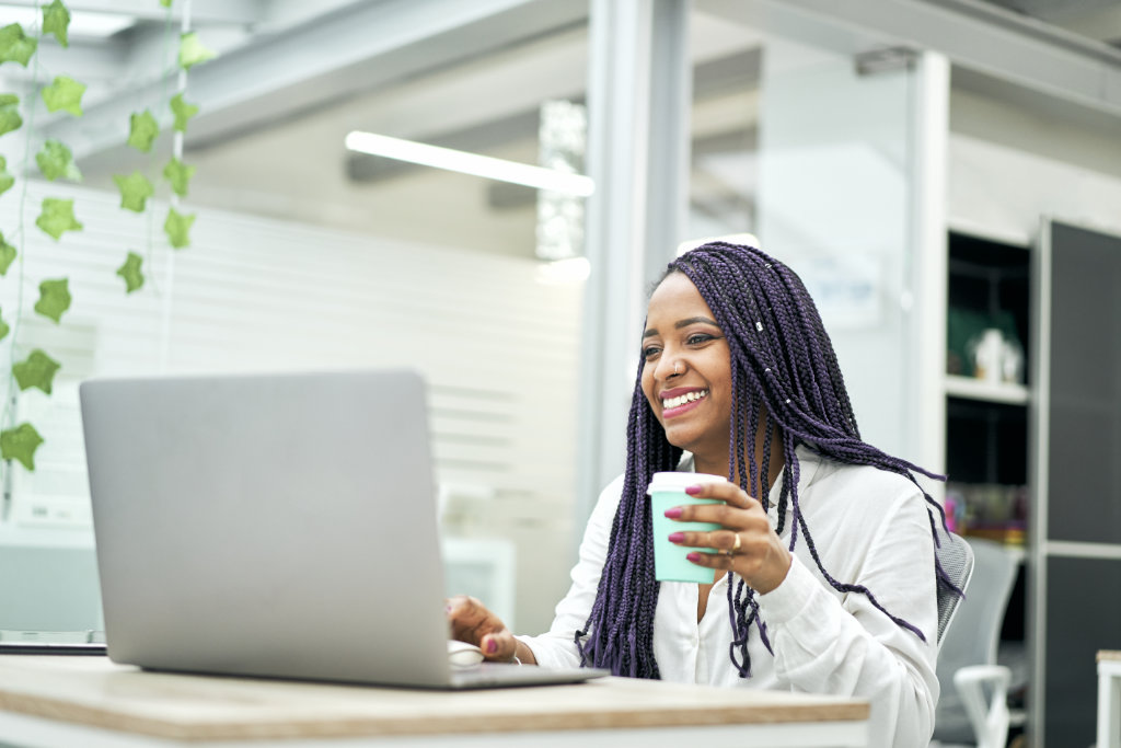 Smiling businesswoman sitting at office desk holding coffee whil